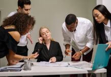 group of people standing beside the woman sitting at the desk